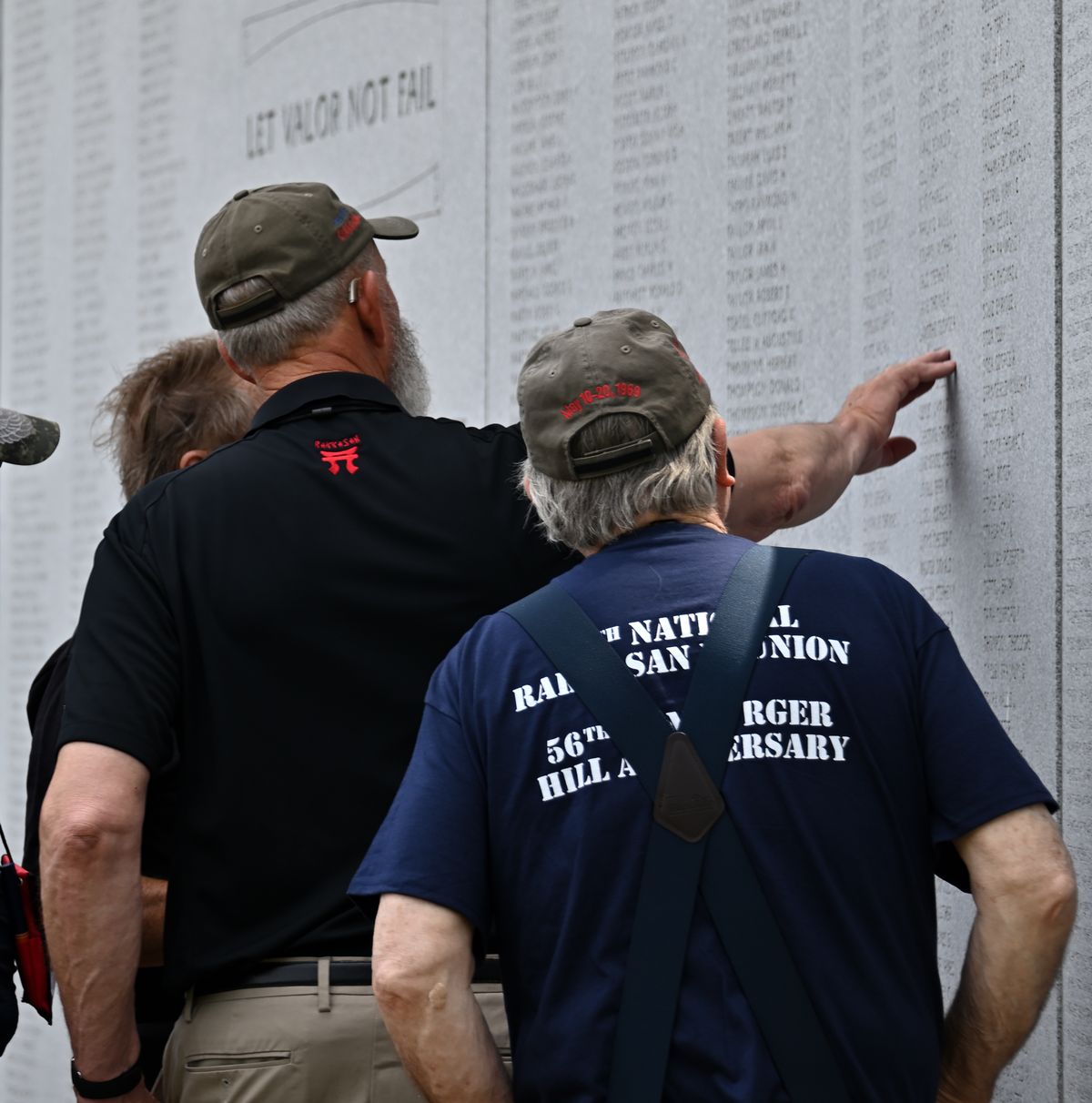 A veteran reaches for a name on a memorial wall during a reunion
